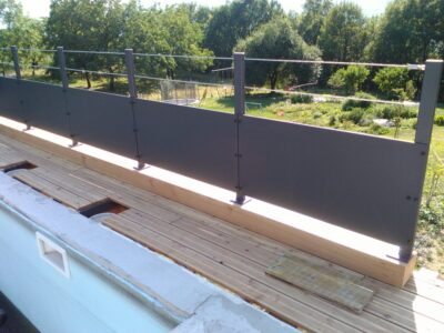 Garde-corps de terrasse en tôle pleine et main courante, face à un jardin