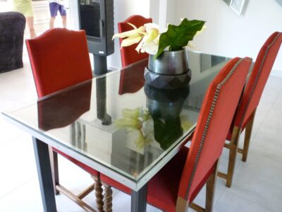 Table de repas à plateau de verre et piétement acier, entourée de chaises rouges