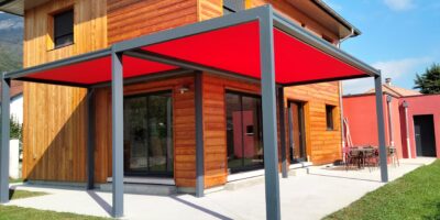 Pergola en acier gris à toile rouge devant une maison à bardage bois