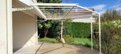 Pergola blanche en acier couvrant une terrasse au bord d'une pelouse
