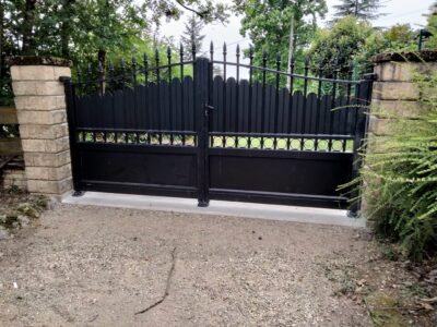 Portail battant en acier noir à barreaudage et pointes, entre deux piliers de pierre